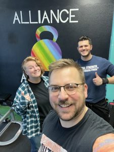 Scott Drapeau and two people with the Alliance Athletics logo in the background