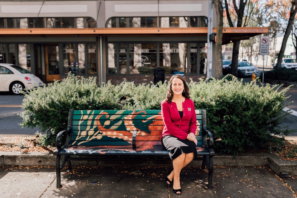 Sandy DiBernardo sitting on a bench by a street in Olympia