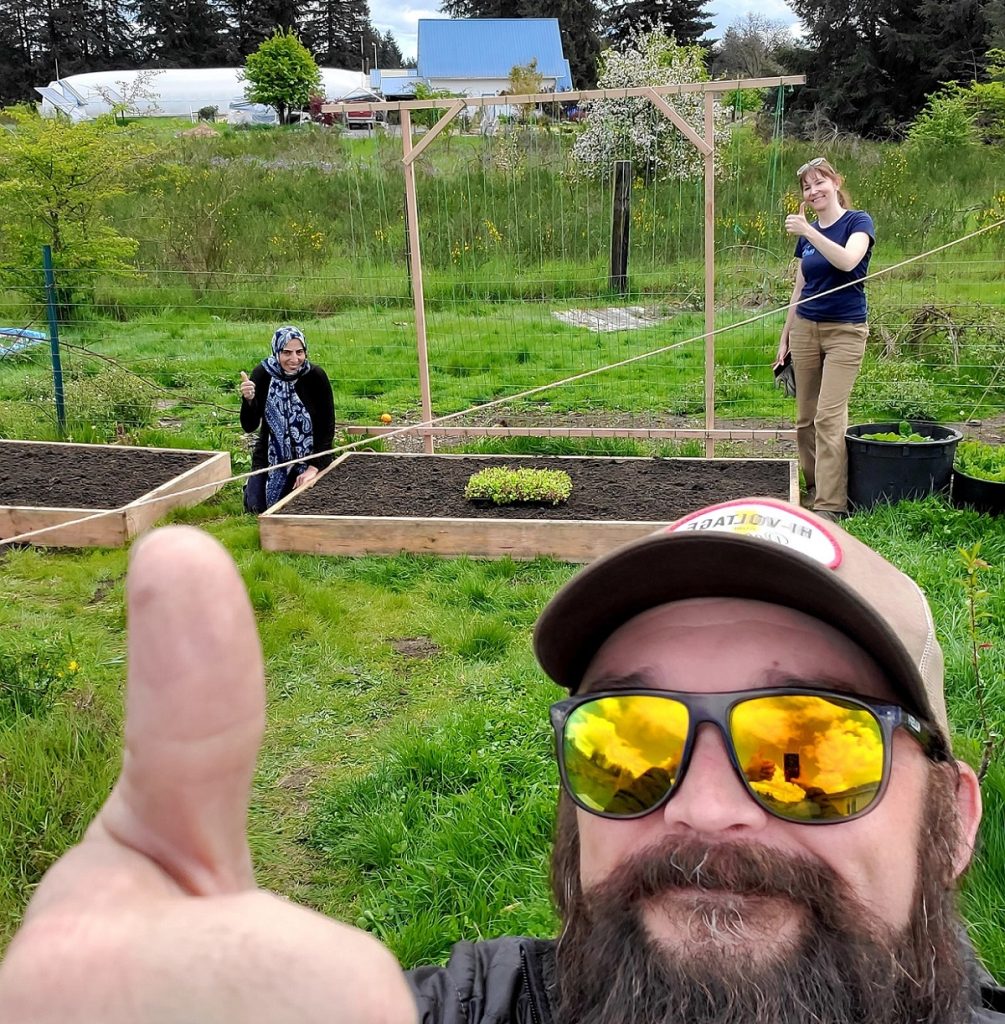 man giving the thumbs up with two woman gardening in the background also giving the thumbs up at GRuB