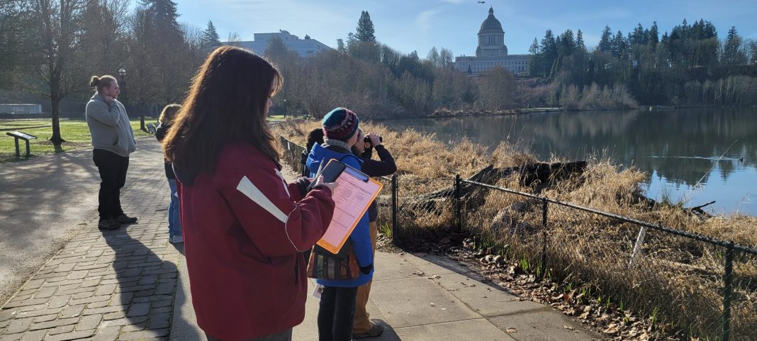 a group of people looking through binoculars and at maps at the Puget Sound Estuary in Olympia