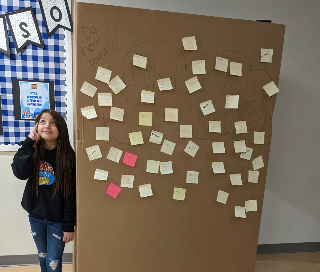 student standing next to a large brown cardboard box covered with post-its, with the vending machine inside