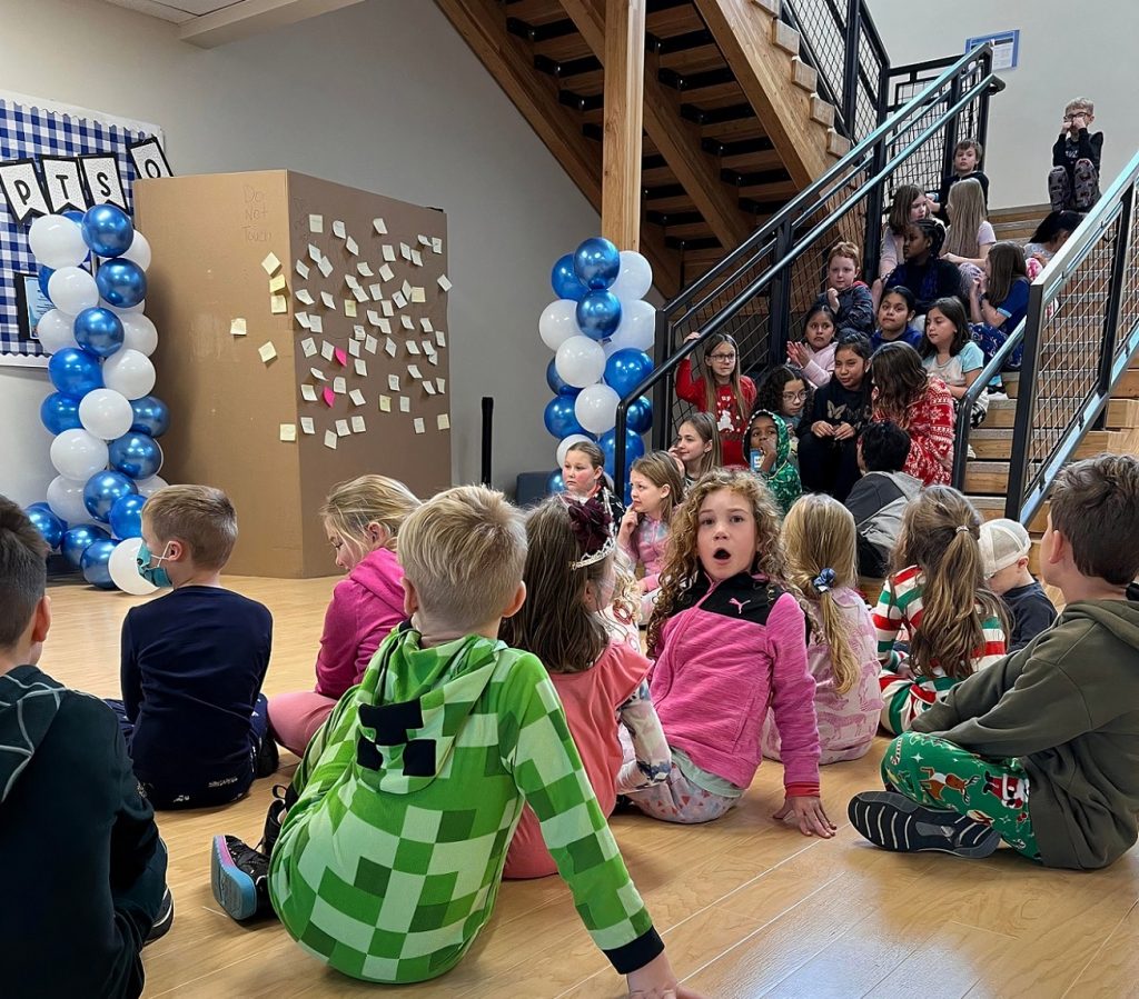 Mountain View Elementary students sitting on the ground and on the staircase waiting to have the cardboard box removed.