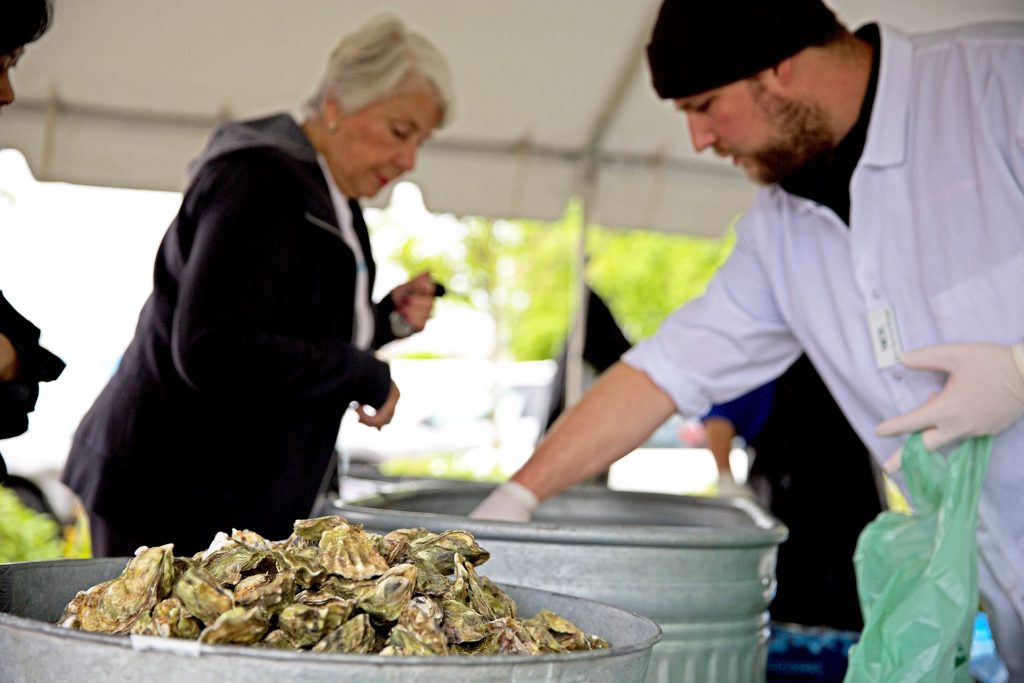 Thriftway worker setting out clams and osyers in a tent with a customer looking on