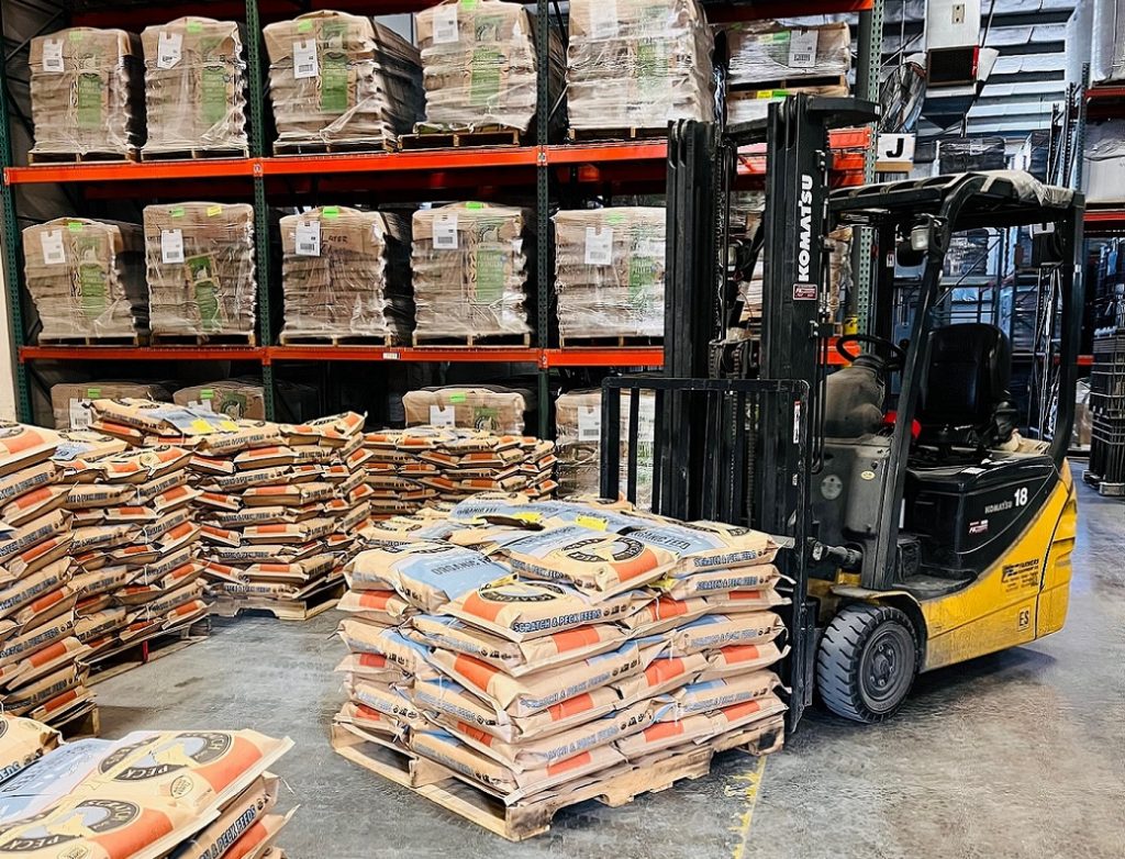 a forklift in a warehouse with Scratch and Peck feed bags on the forks, on the floor, and on the shelves