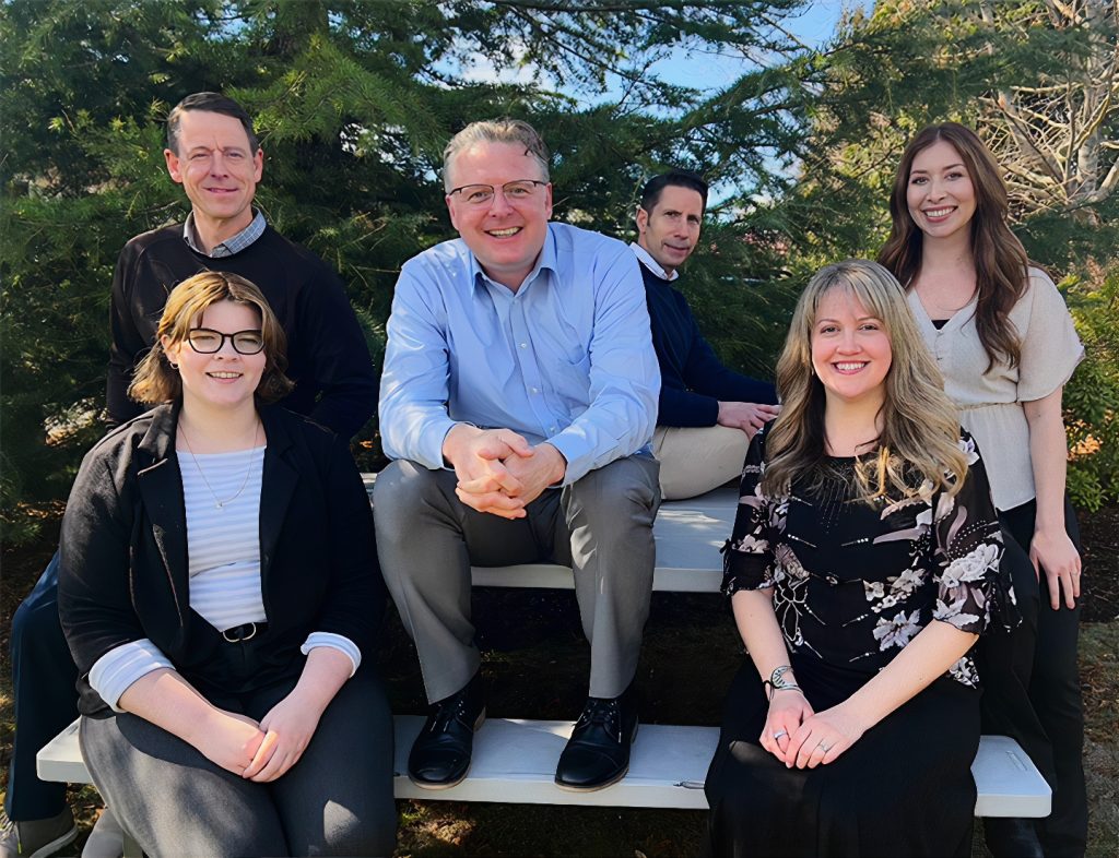 Group photo of Bank of the Pacific team members sitting on a picnic table with Jay Johnston in the middle