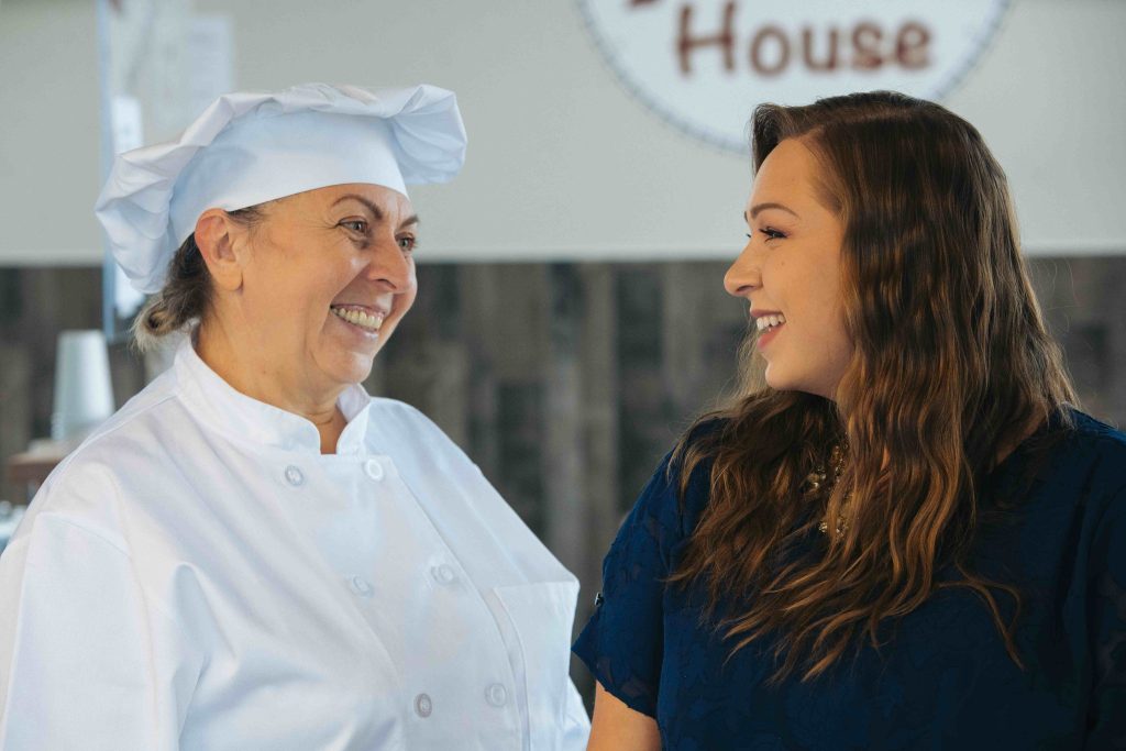 a women in a chef's hat smiling at a woman in a navy shirt as they look at each other