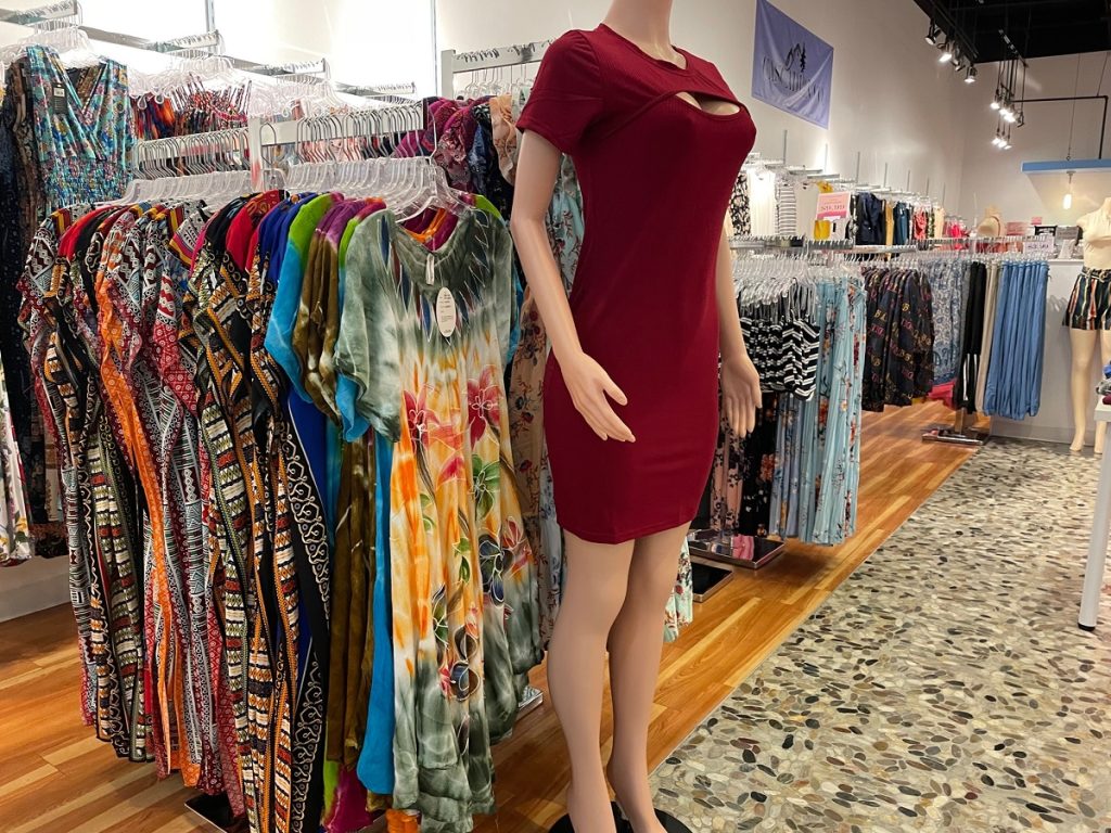a mannequin with a dress on and rack of clothes behind it