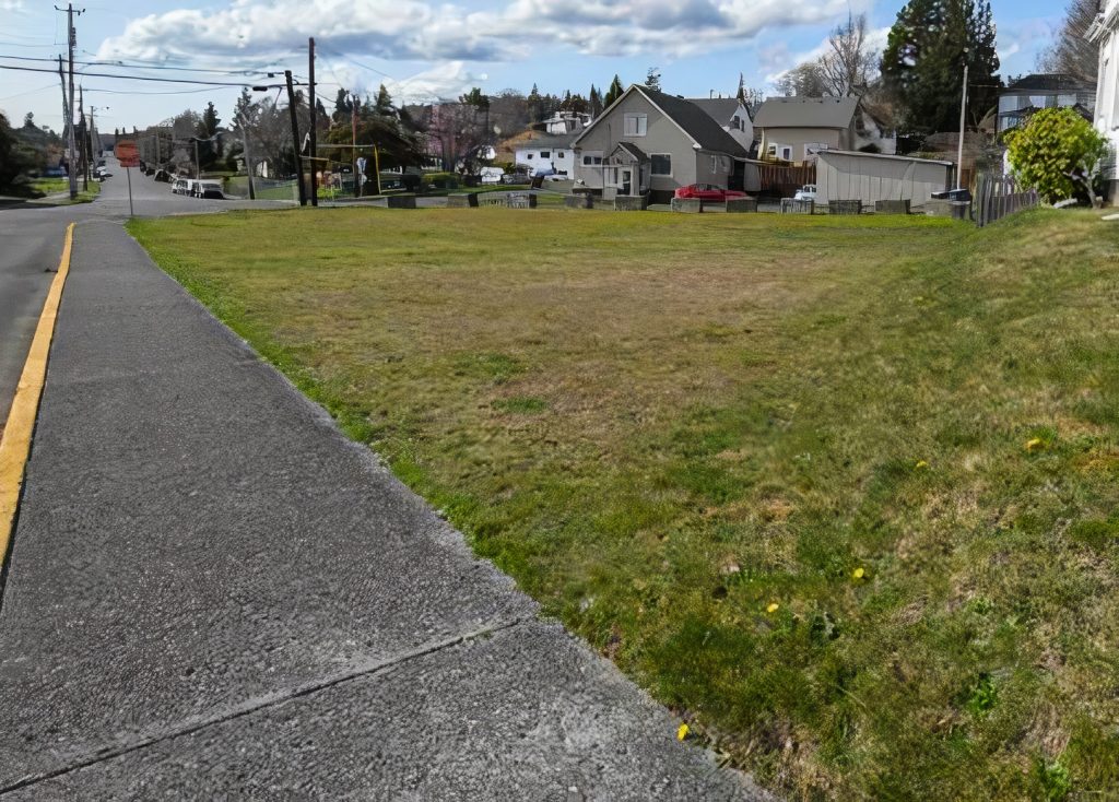 concrete sidewalk and green space with housing in the distance