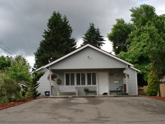 Grey house with a large driveway and trees behind it