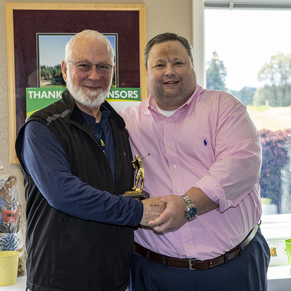 A man giving another man a small golfing trophy