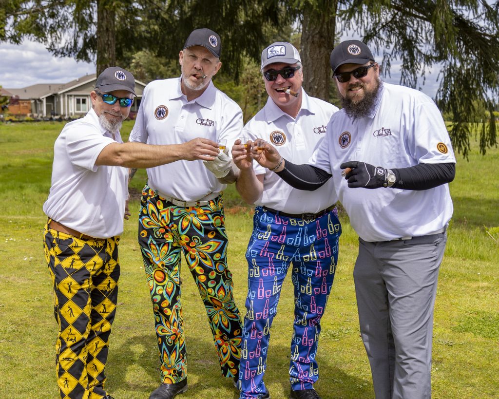 Four golfers dressed in loud pants sharing shots and cigars