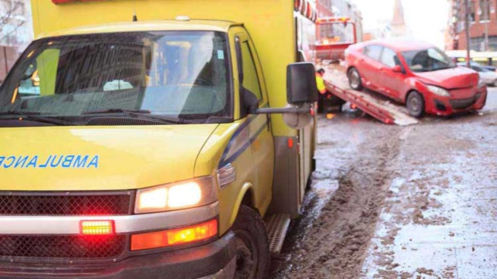 yellow ambulance with a red car being put on a tow truck in the background