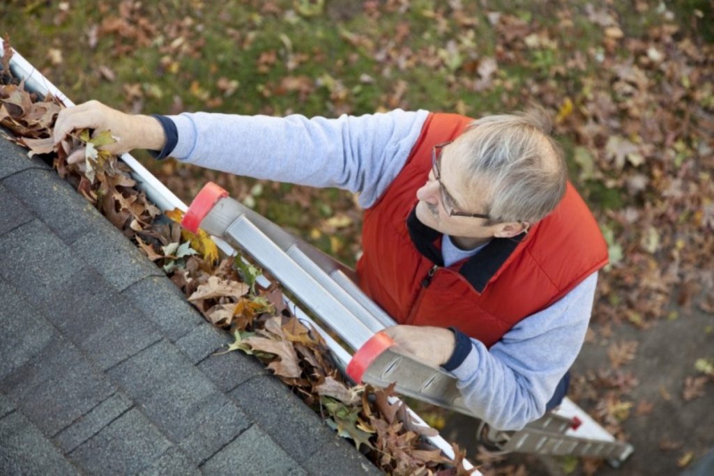 grey-haired man on a ladder looking at a roof of a house