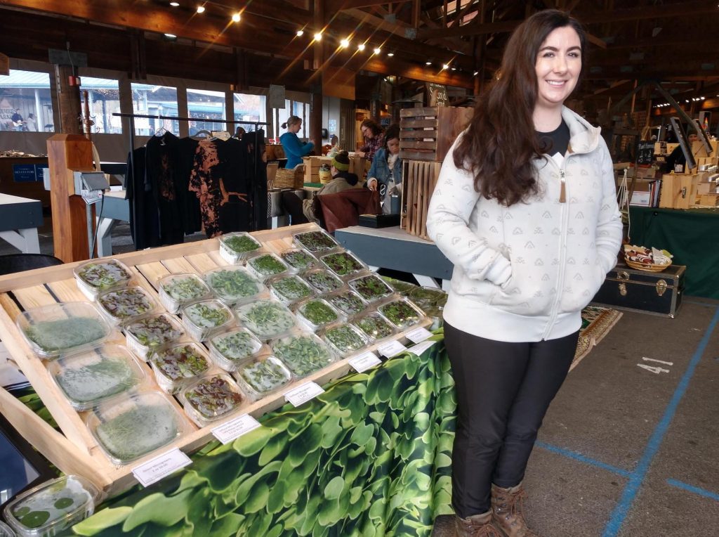Norah Montoya standing next to her booth with microgreens in it at Olympia Farmers Market