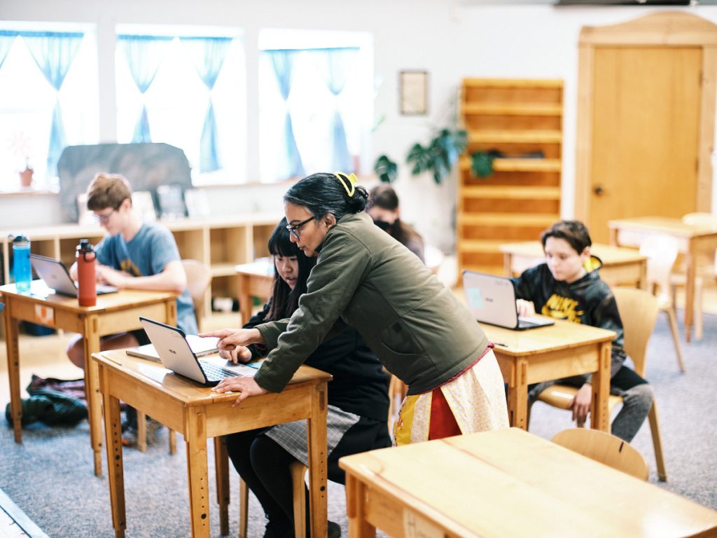 a teacher helping a student at their desk with a laptop