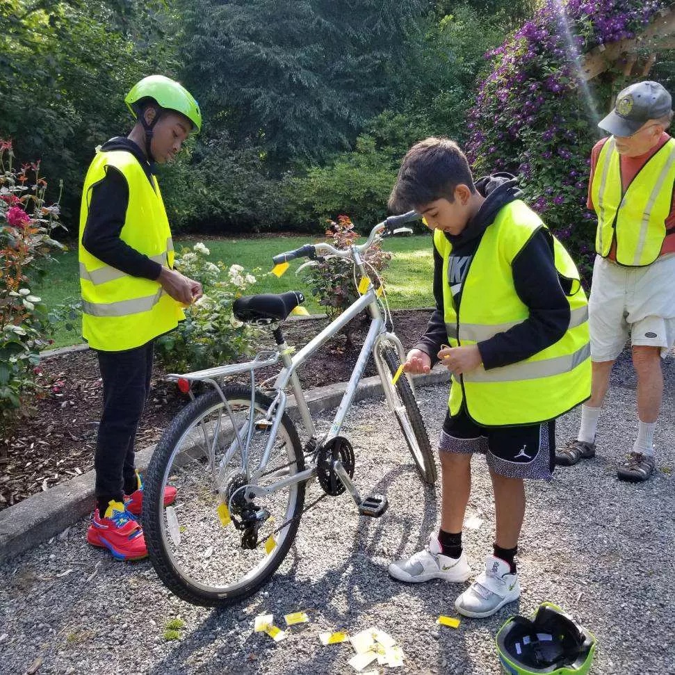 two kids outside labeling parts of a bike with an instructor watching