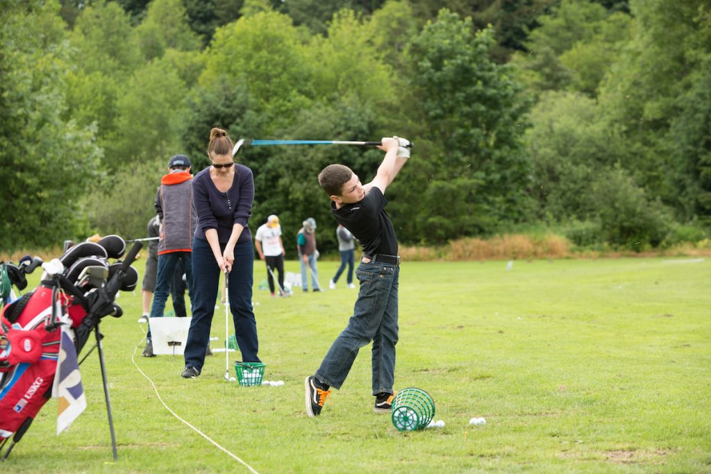 a line of young kids hitting golf balls with clubs