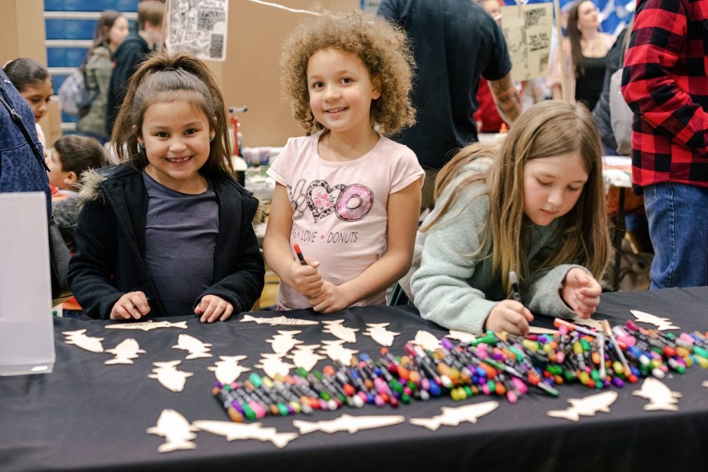 three girls at a table with white paper fish and crayons