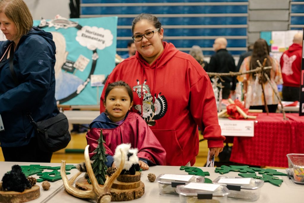 Women and a child, standing at a table with green wooden birds, smiling at the camera