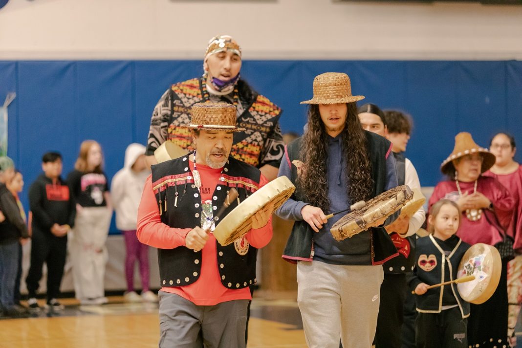 a group off men, women and children playing types of Native American drums in front of a crowd