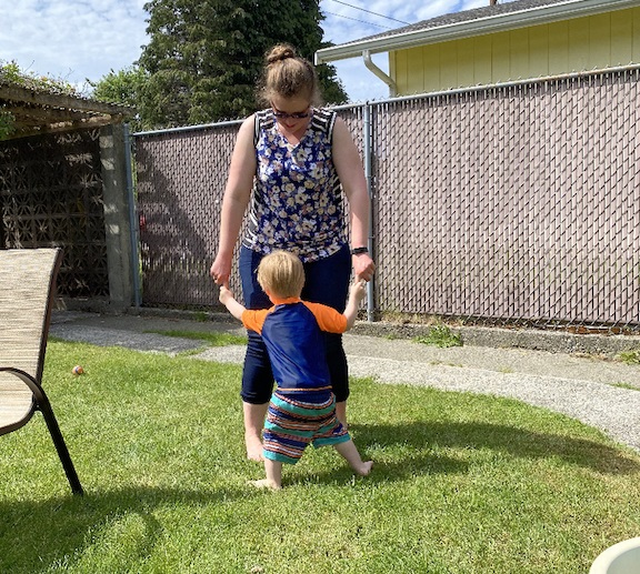 a women holding both hands with a toddler in a backyard