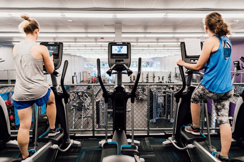 two women on ellipticals with an empty elliptical between them