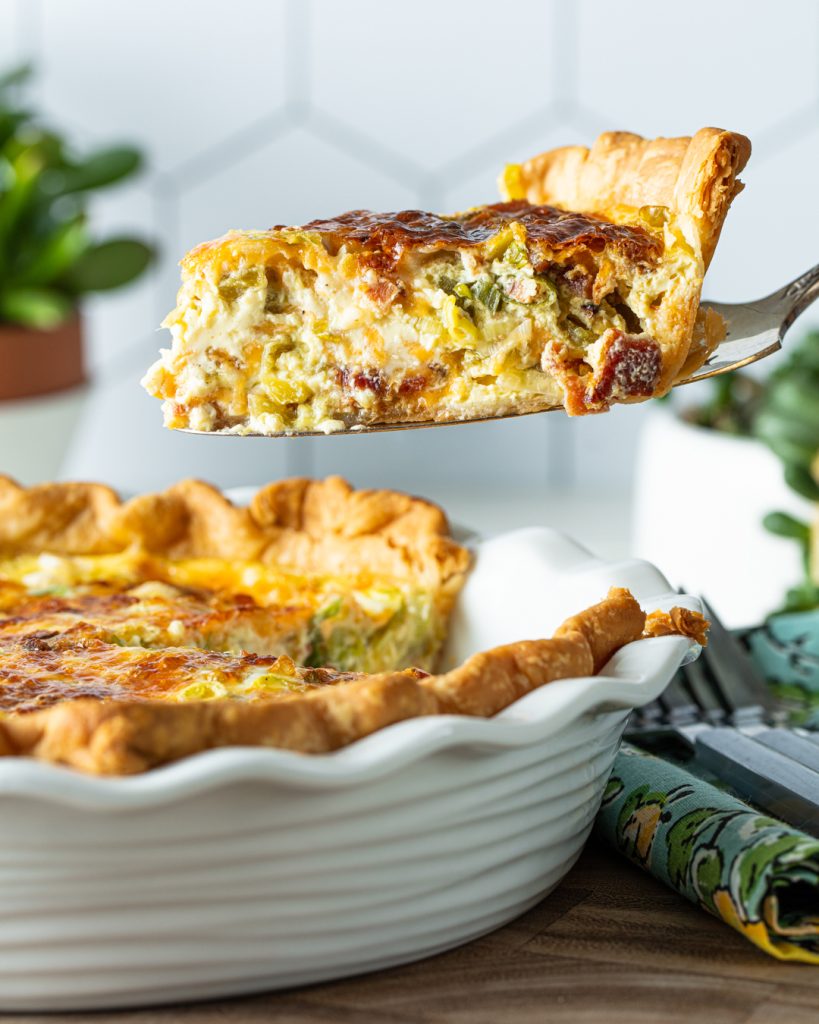 Large quiche in a white baking pan with a slice being taken from it