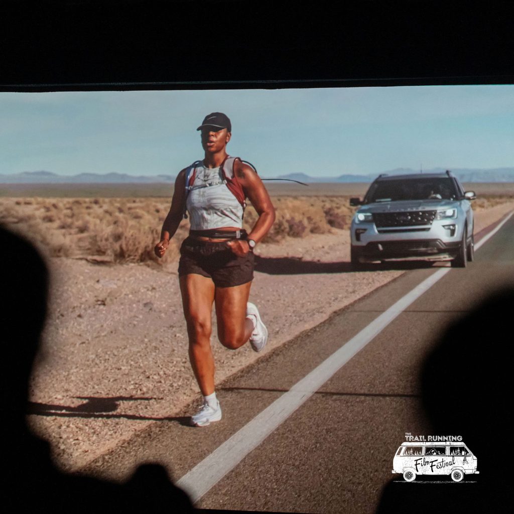 image of people running on a road with a car behind on a big theater screen