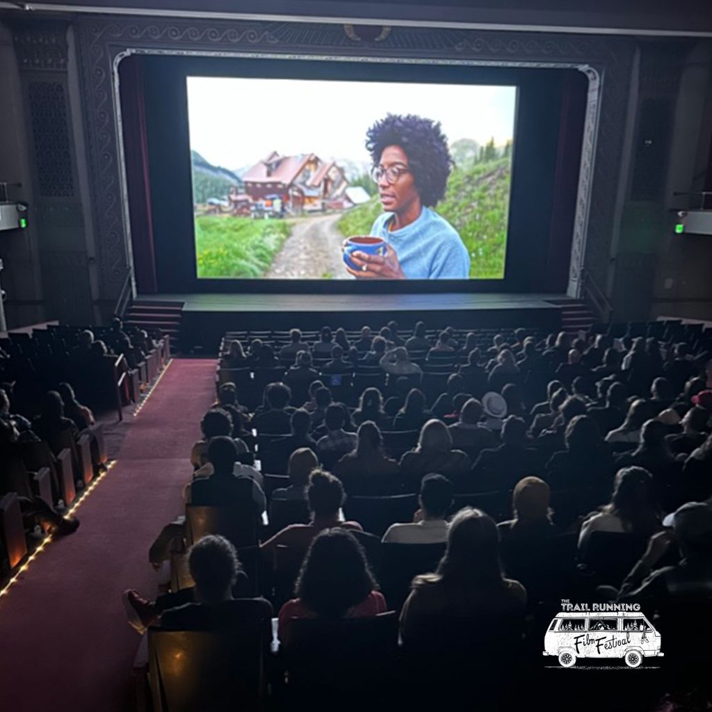 Photo of a woman holding a cup of coffee with a cabin in the background on a big screen in a theater