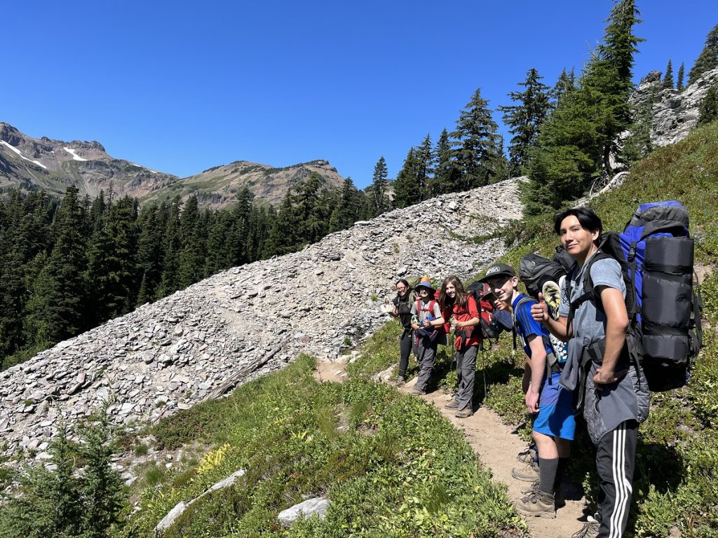 children hiking up a grassy hill with an adult 