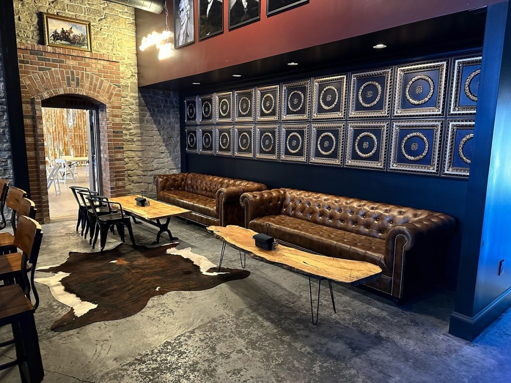 two large leather couches with raw rood tables and a cowhide are in front of a brick archway leading to an open room with tables and chairs