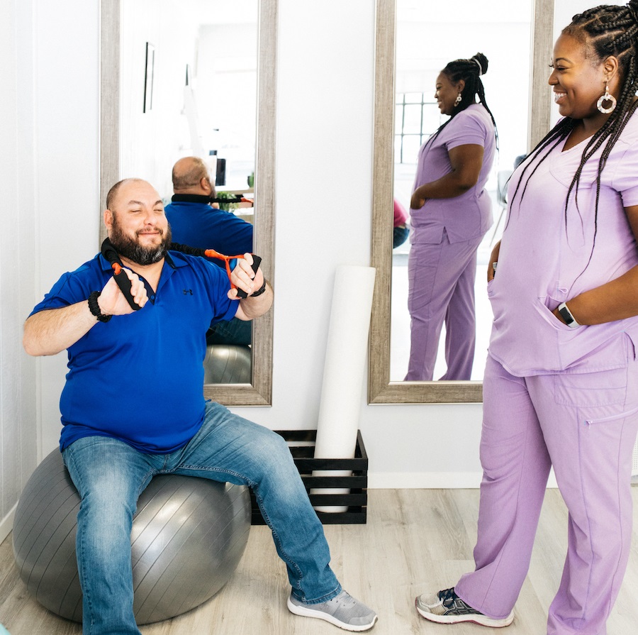 man on an exercise ball with resistance bands looped behind his neck being held by both hands while Dr. Cordis stands next to him