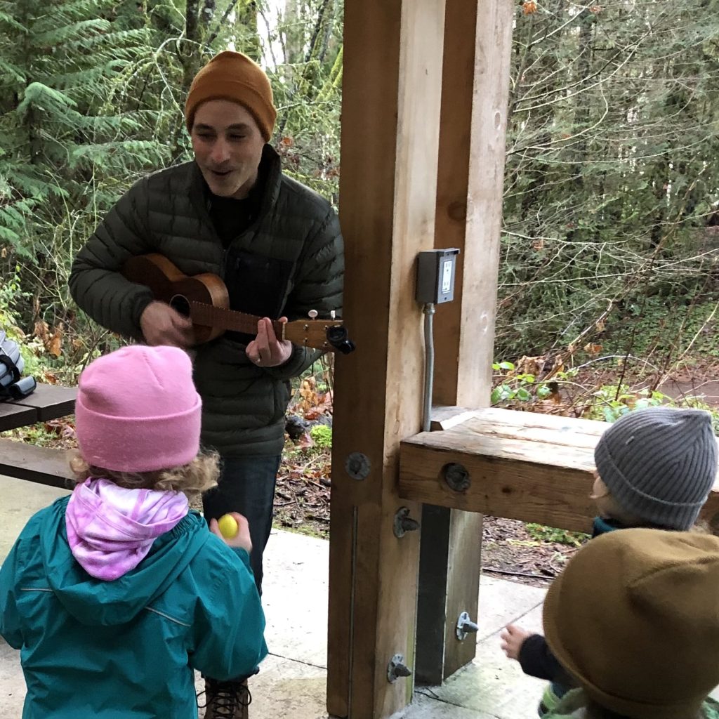 Chris Sabatini playing a ukele in a structure in the woods to some kids