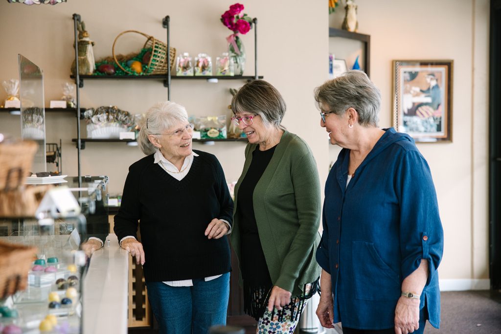 Three women talking and smiling at a counter of a shop.