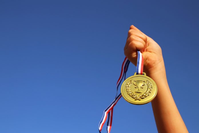 child hand raised, holding gold medal against sky. education, success, achievement, award and victory concept.