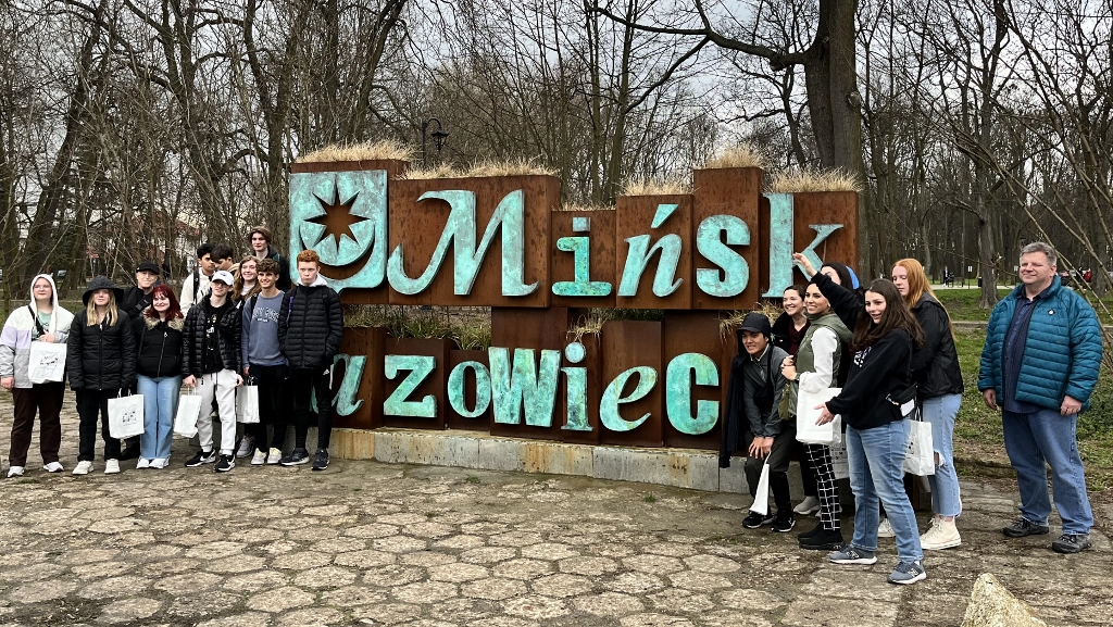 North Thurston High School students standing on either side of a large wood sign outside that says, 'Minsk' and another word partially obscured.