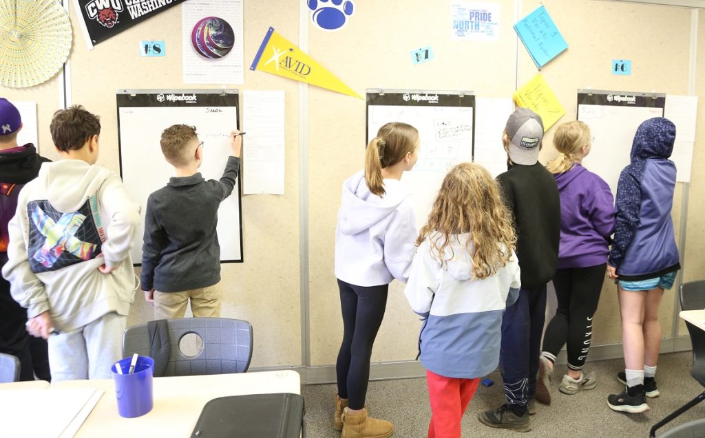 Kids gathered around whiteboards in a classroom working on math problems at North Thurston Public Schools