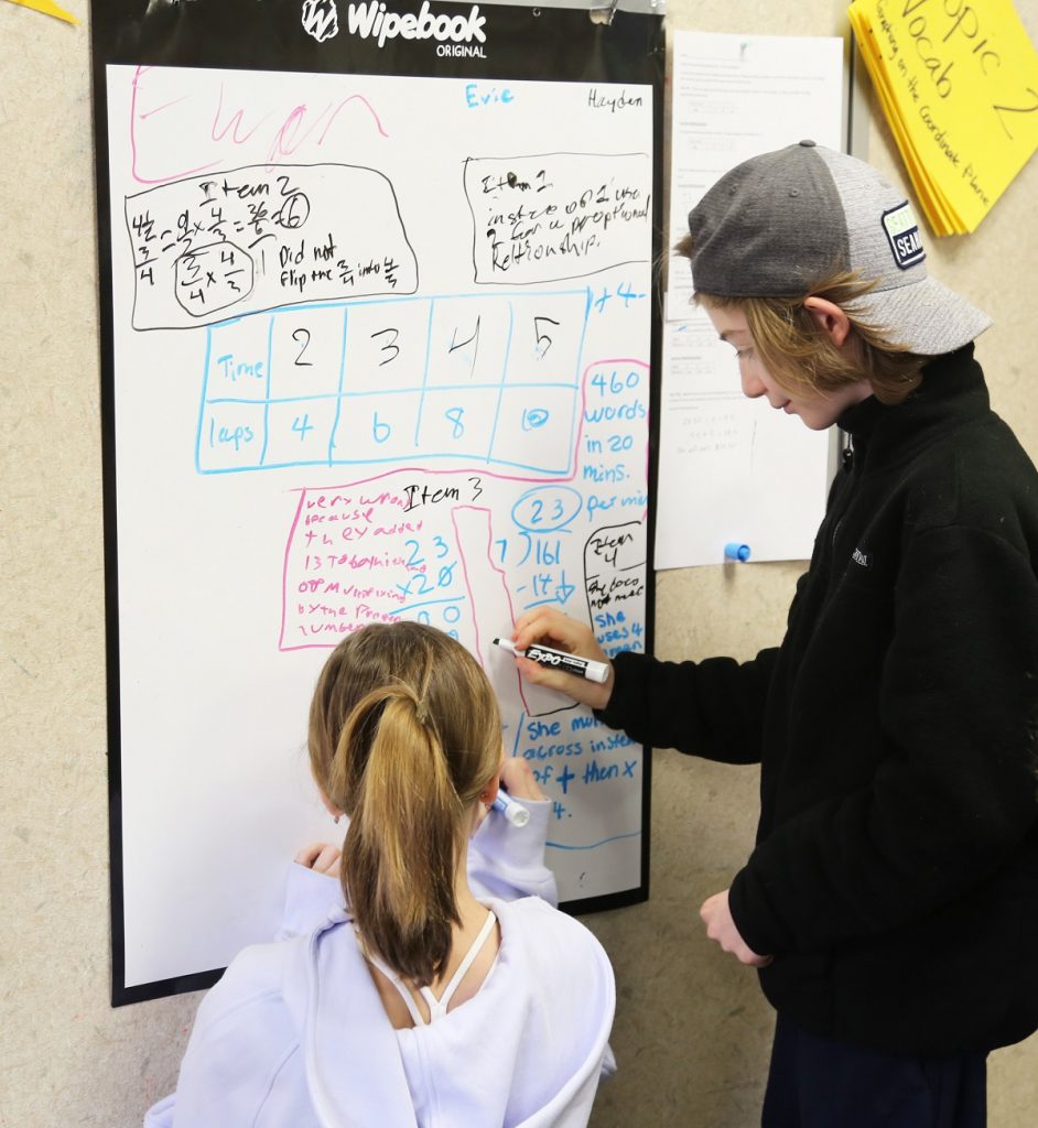 two kids gathered around whiteboards in a classroom working on math problems at North Thurston Public Schools