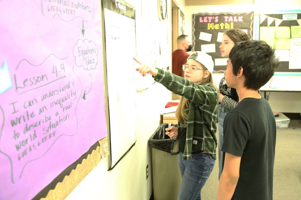 Kids gathered around whiteboards in a classroom working on math problems at North Thurston Public Schools