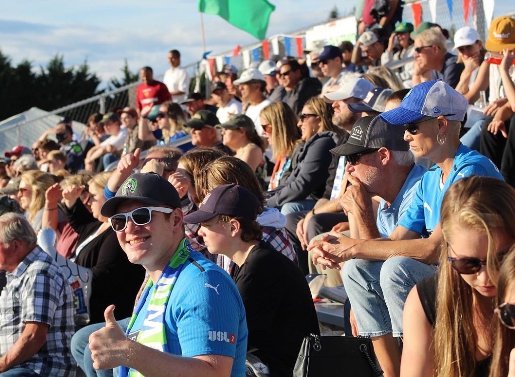 crowd of people watching a soccer game on a sunny day