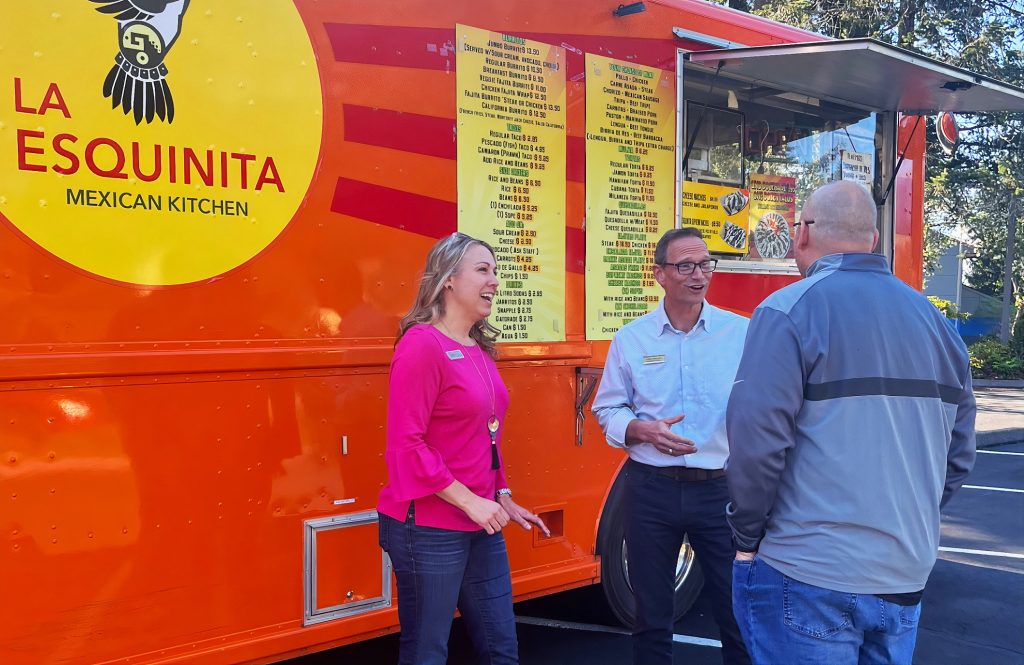 Three people standing outside a red and yellow taco truck