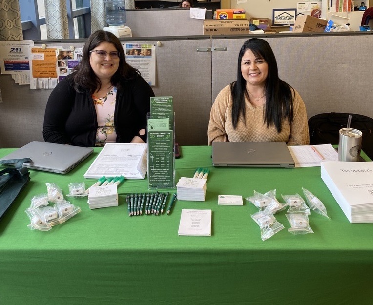 two women sitting behind a table with a green tablecloth and brochures on it.