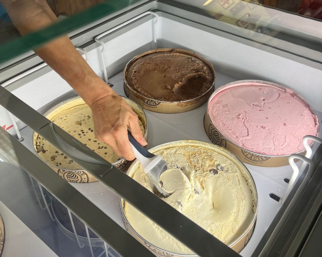 a hand scooping ice cream with a scoop from large tubs in a freezer