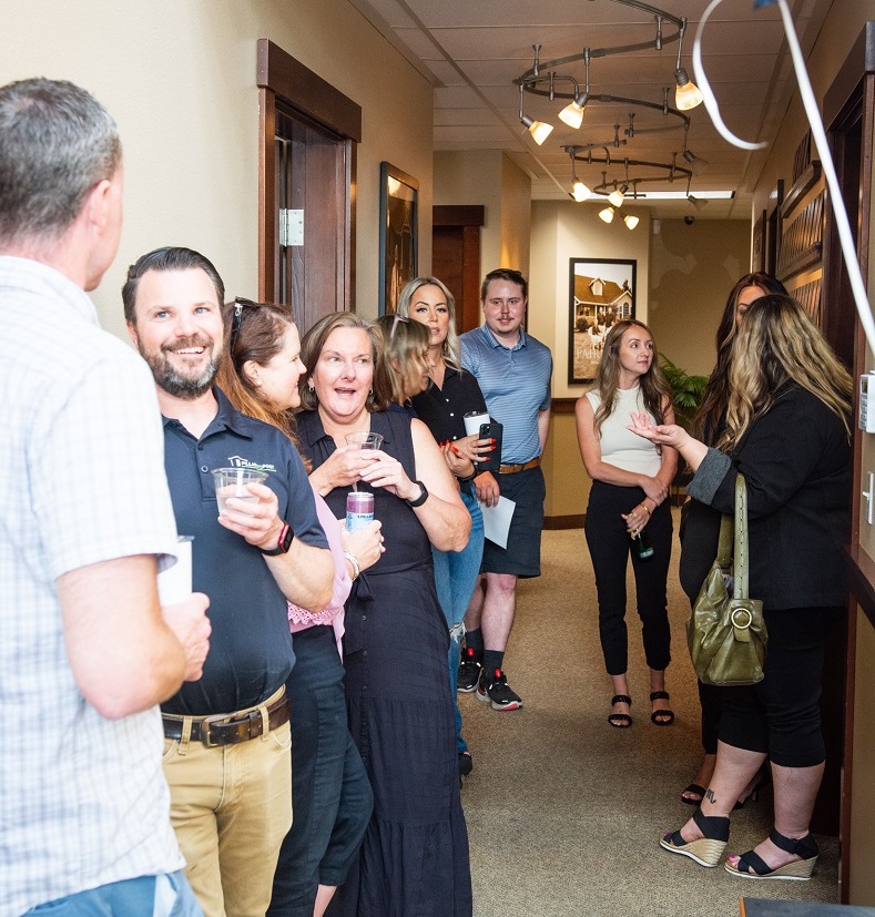 large group of people talking and drinking drinks in a hallway with balloons