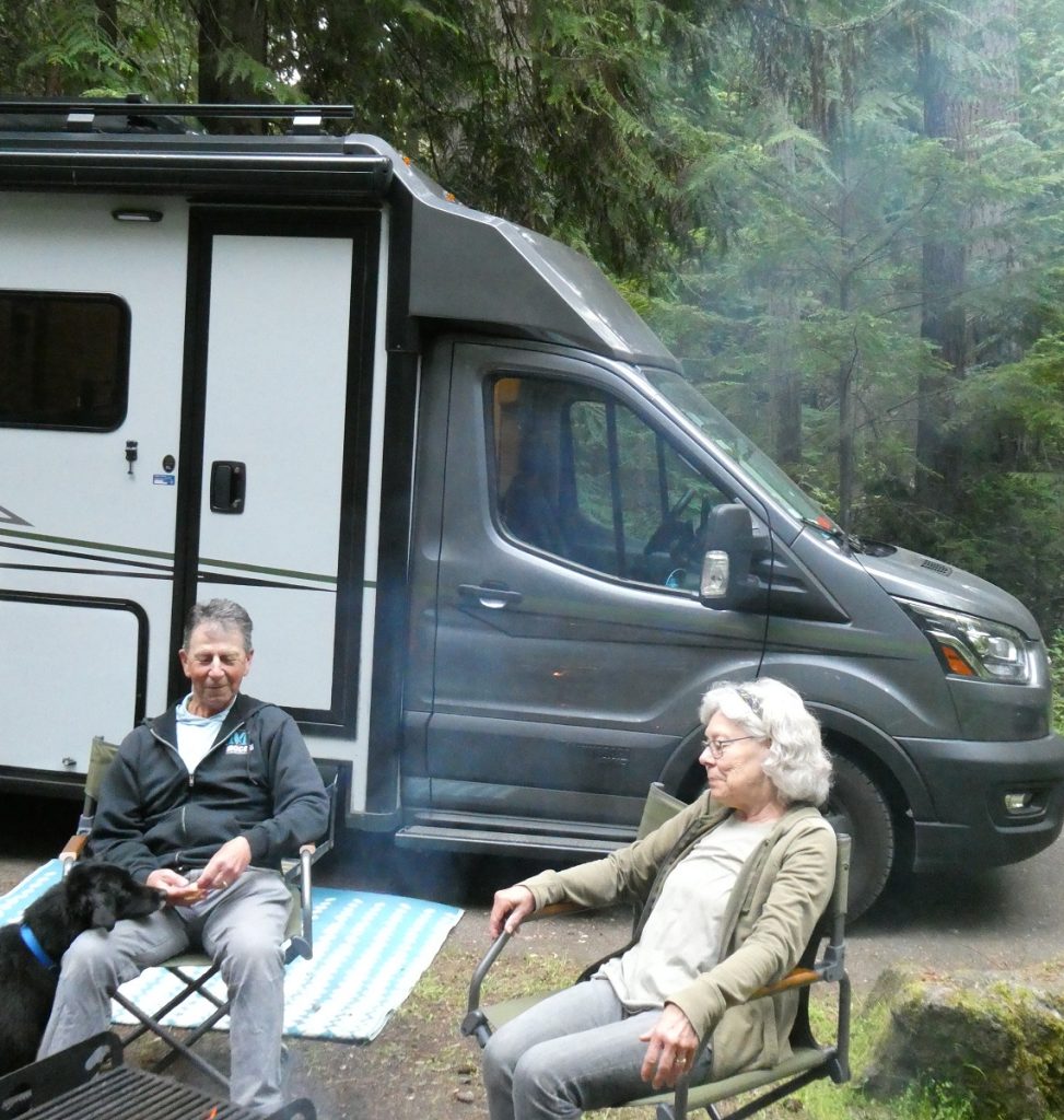 A couple sit in camping chairs outside their RV