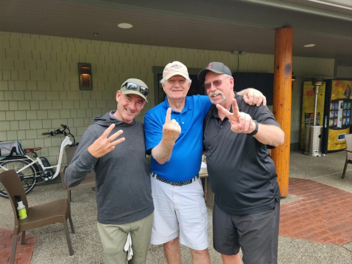 Three men standing together, one holding up one finger, one holding up two fingers and one holding up three fingers