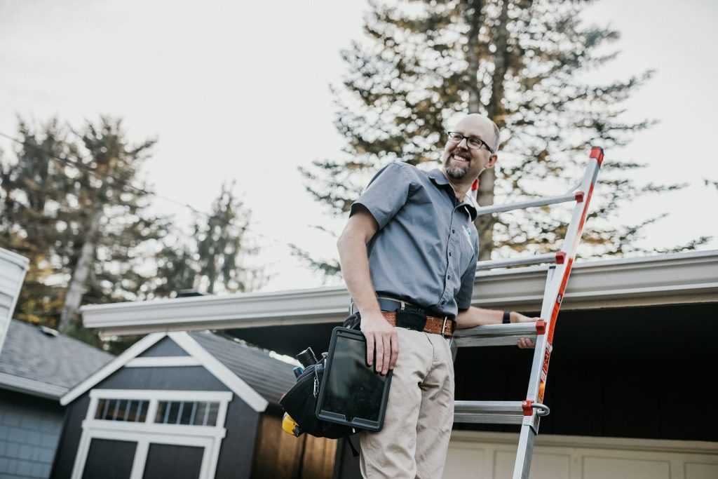 Boggs Inspection technician smiling on a ladder against a house