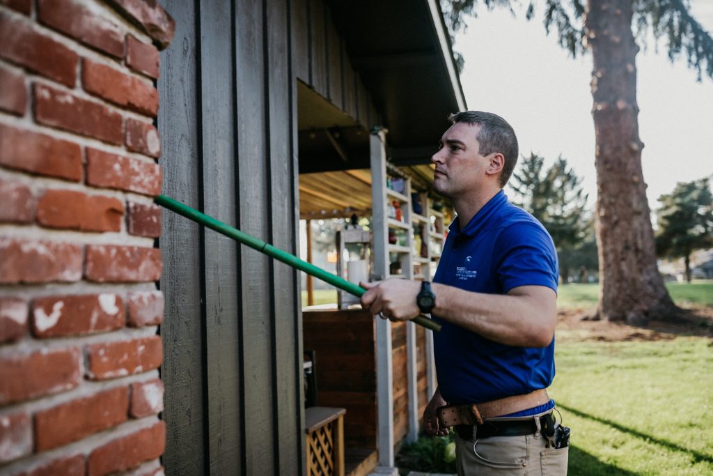 Boggs Inspection technician with a green pole against the side of a house
