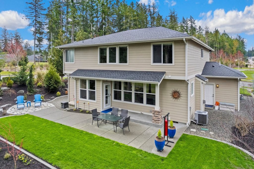 exterior shot of a beige, two story home with a grass backyard and patio with a table and chairs