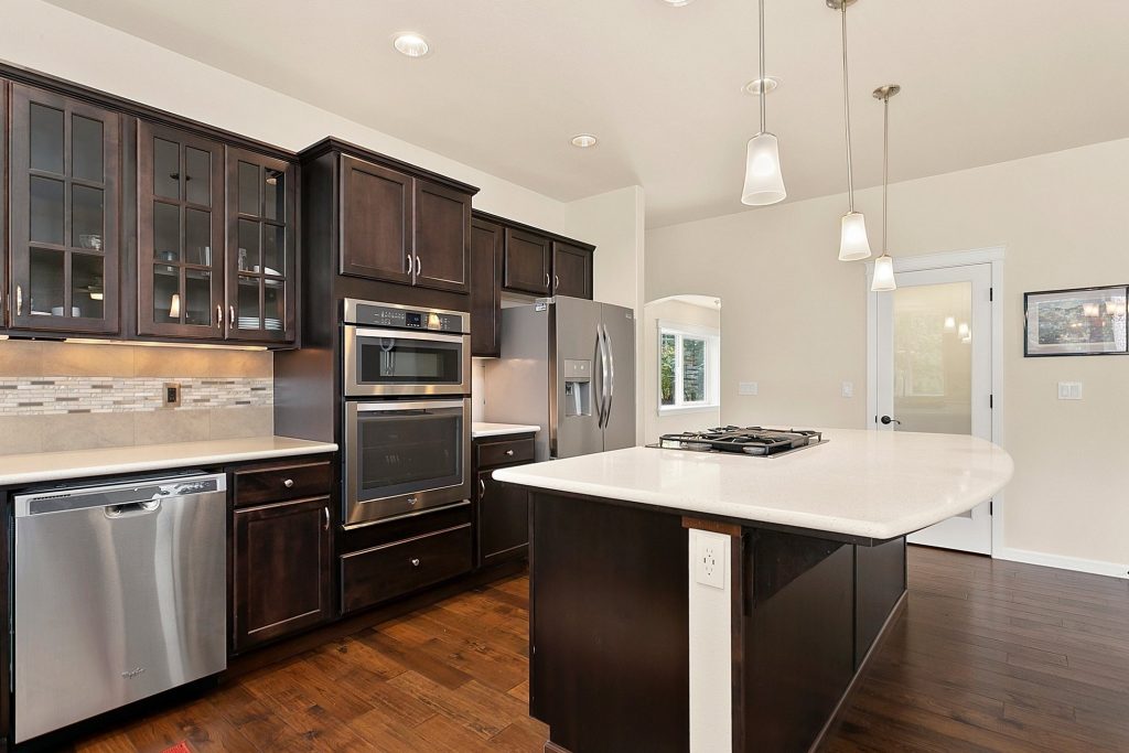 Kitchen with wood floors, dark brown cabinets, light counter topcs and stainless steel appliances and an island.